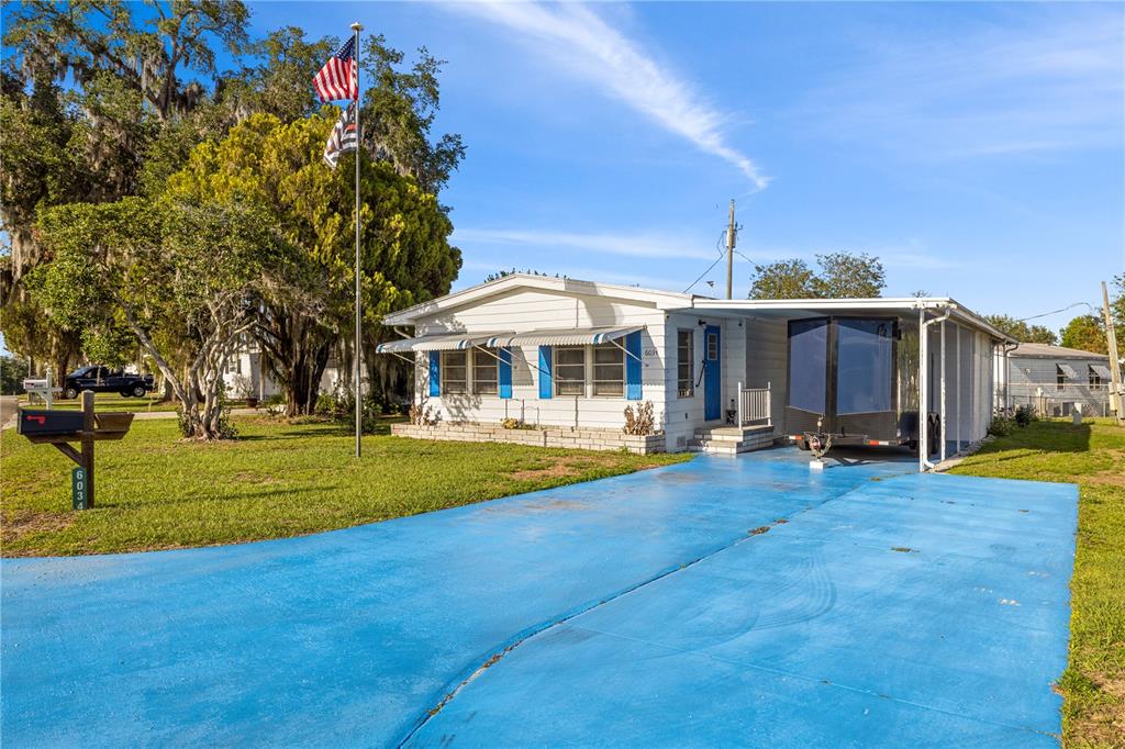A single-story mobile home with a bright blue driveway and a carport — 6034 ALPINE DRIVE, ZEPHYRHILLS, FL