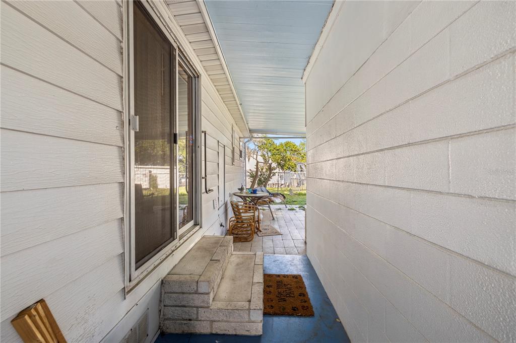 A covered outdoor walkway leads to a patio area with a sliding glass door — 6034 ALPINE DRIVE, ZEPHYRHILLS, FL