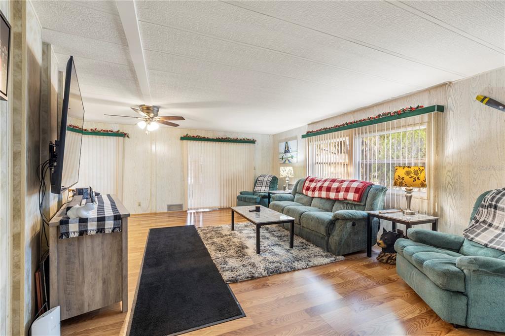 A living room features wood-paneled walls, a green sofa, two armchairs, and wood flooring — 6034 ALPINE DRIVE, ZEPHYRHILLS, FL