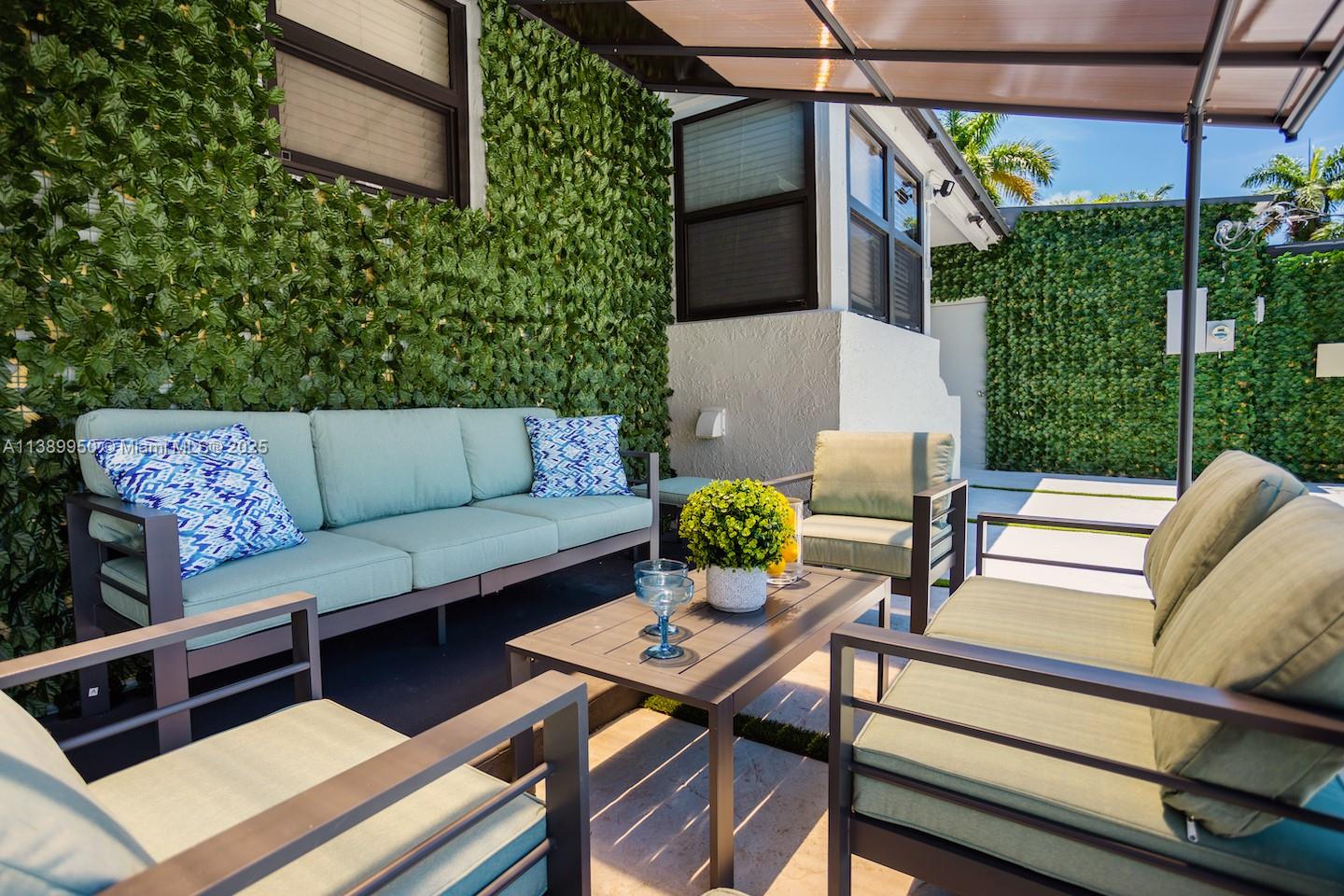 An outdoor patio features modern metal furniture with light green cushions against a green wall — 801 Harrison St, Hollywood FL 33019, HOLLYWOOD, FL