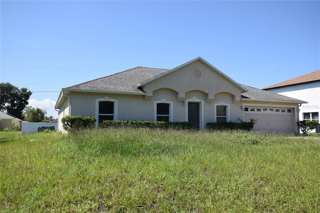 A single-story house with a tan stucco exterior, a shingled roof, and an overgrown lawn — 3785 TRADE STREET, DELTONA, FL