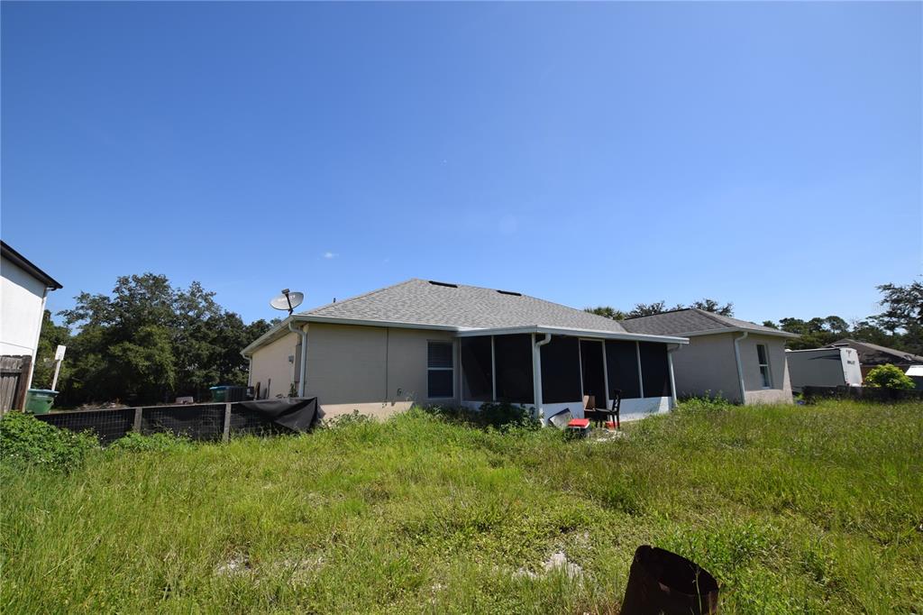 The exterior rear view of a house features a screened-in porch and an overgrown yard — 3785 TRADE STREET, DELTONA, FL