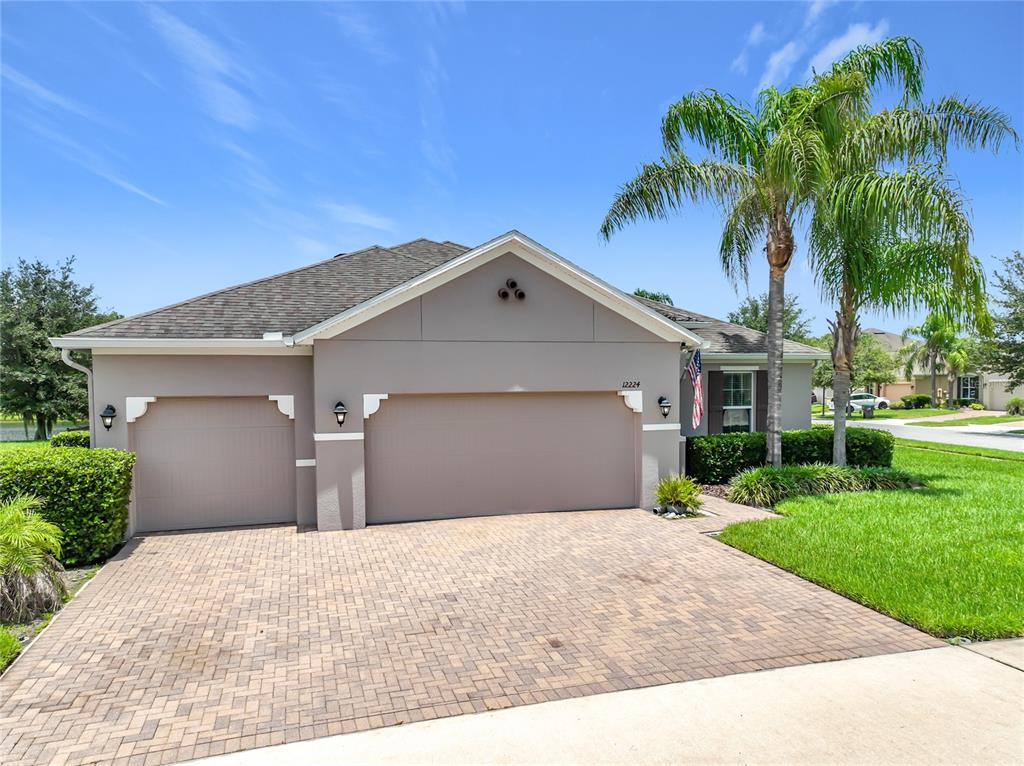 A single-story house with a three-car garage and a paved driveway under a blue sky — 12224 STONE BARK TRAIL, ORLANDO, FL