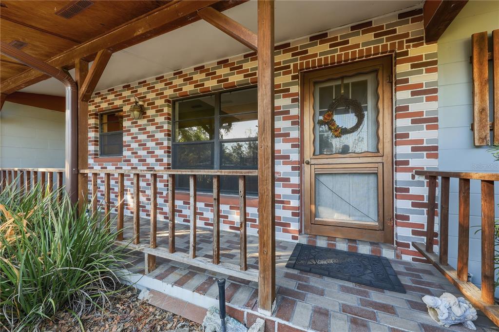 A covered front porch features a brick facade, wooden railings, and a wooden screen door — 3809 NEEDLES DRIVE, ORLANDO, FL