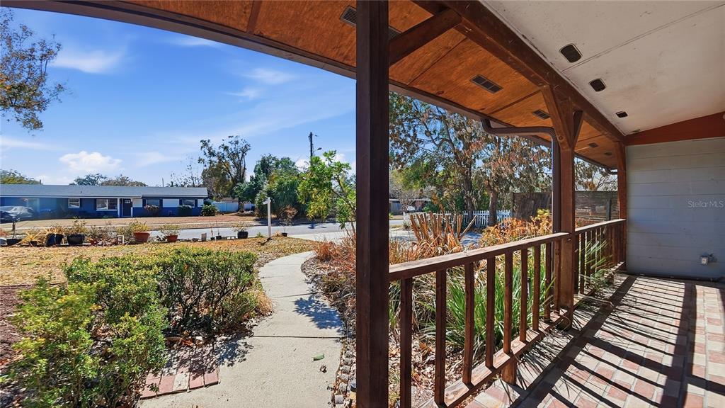 A covered porch with a wooden railing overlooks a front yard and a neighboring house — 3809 NEEDLES DRIVE, ORLANDO, FL