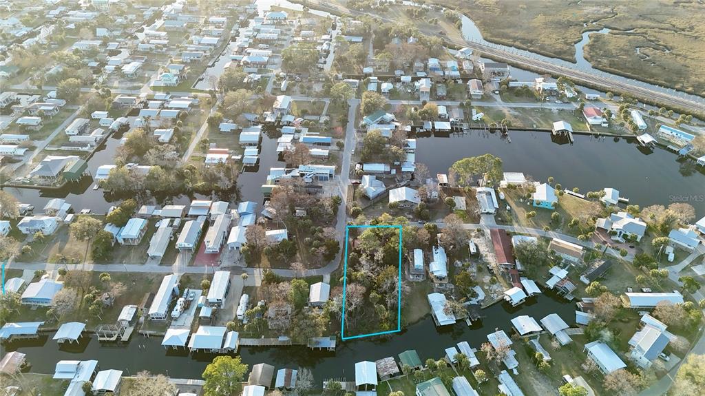 An aerial view shows a vacant, tree-covered lot outlined in blue within a waterfront neighborhood — 12 SE 241ST STREET, SUWANNEE, FL