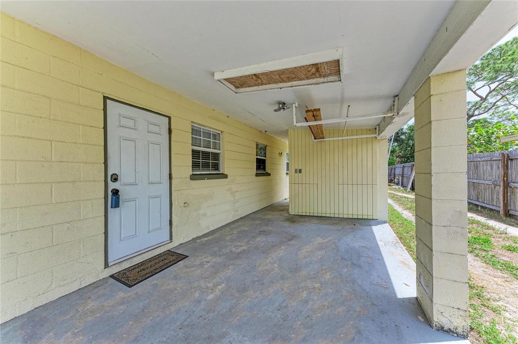 A covered concrete patio features a white door, yellow block walls, and an exposed ceiling — 2564 WOOD STREET, SARASOTA, FL