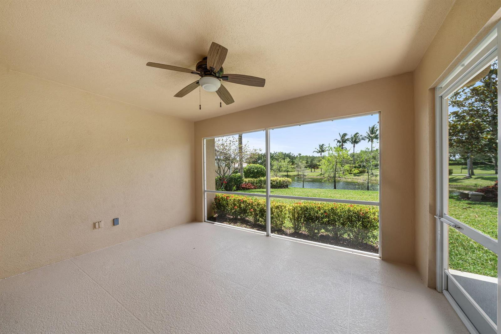 A sunroom with a ceiling fan, beige walls, and large windows overlooking a pond — 3214 Verdmont Lane, Wellington FL 33414, WELLINGTON, FL