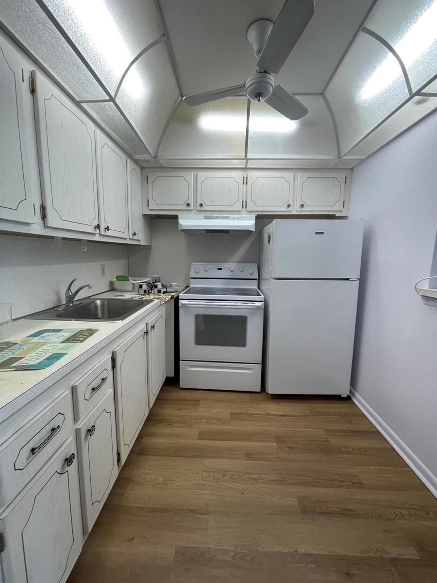 A galley kitchen features white cabinets, white appliances, a stainless steel sink, and wood-look flooring — 522 Tilford X # 522, Deerfield Beach FL 33442, DEERFIELD BEACH, FL