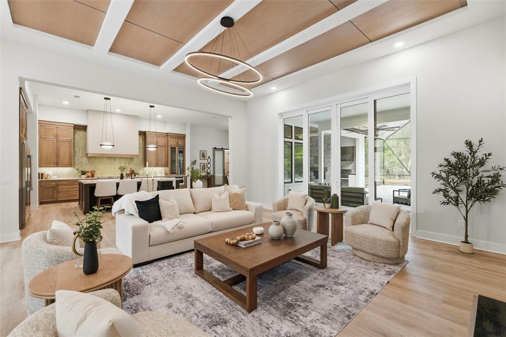 A living room with a coffered wood ceiling, modern chandelier, and open kitchen view — 5995 SW 124TH WAY, ARCHER, FL