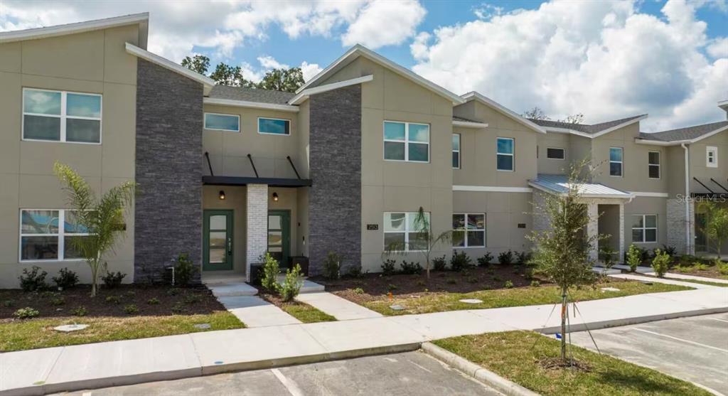 A two-story townhouse exterior features tan siding, stone accents, and a concrete walkway — 2513 READING TRAIL, KISSIMMEE, FL