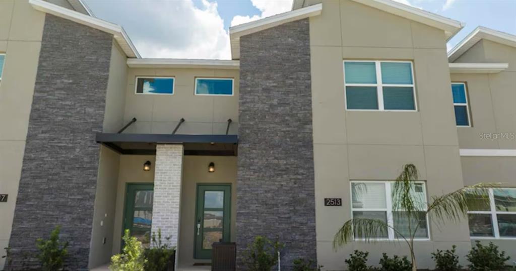 A two-story townhouse exterior features tan stucco walls, stone veneer accents, and green entry doors — 2513 READING TRAIL, KISSIMMEE, FL