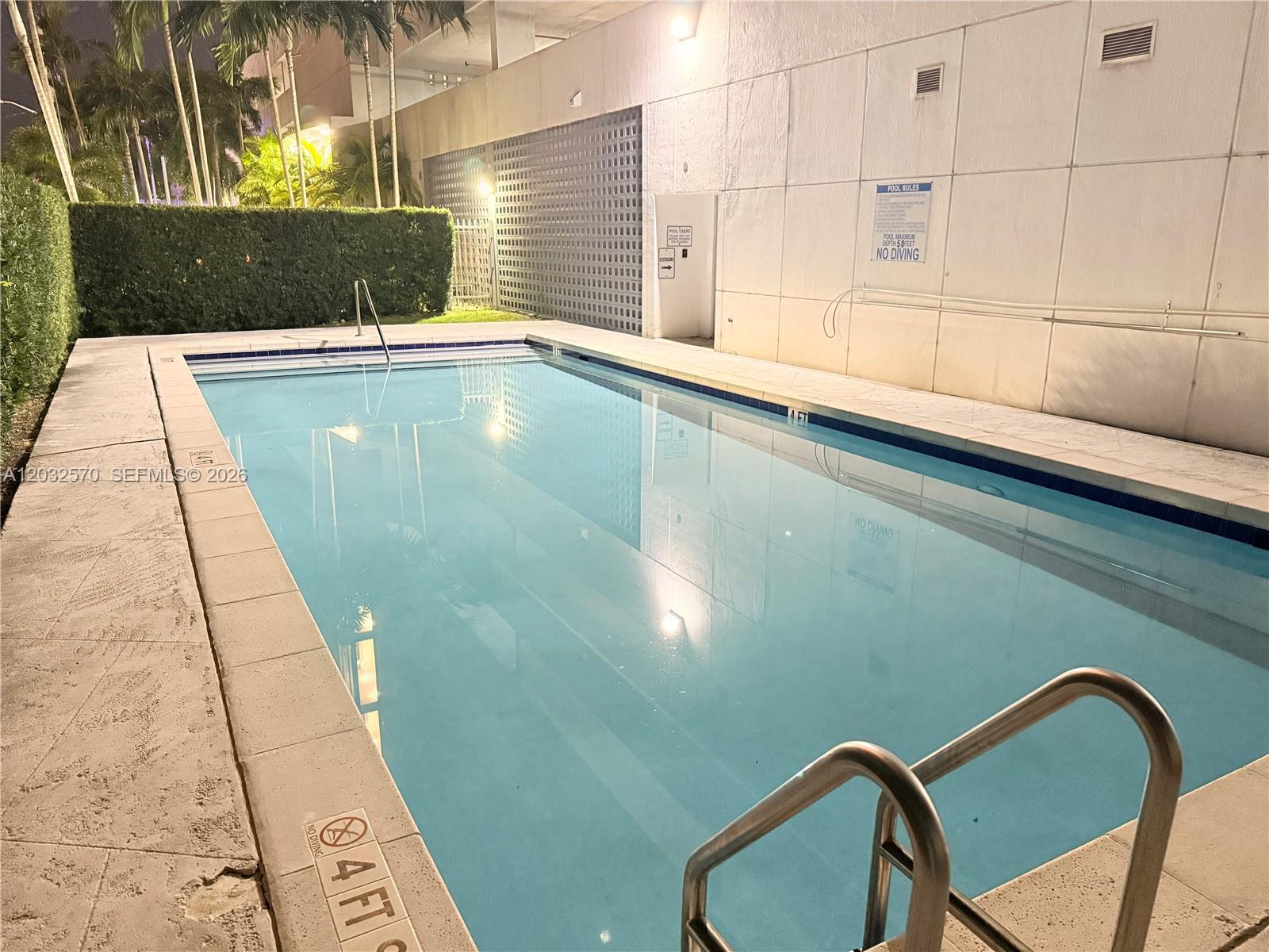 An outdoor rectangular swimming pool is surrounded by a concrete deck and a white wall — 36 NW 6th Ave # 601, Miami FL 33128, MIAMI, FL