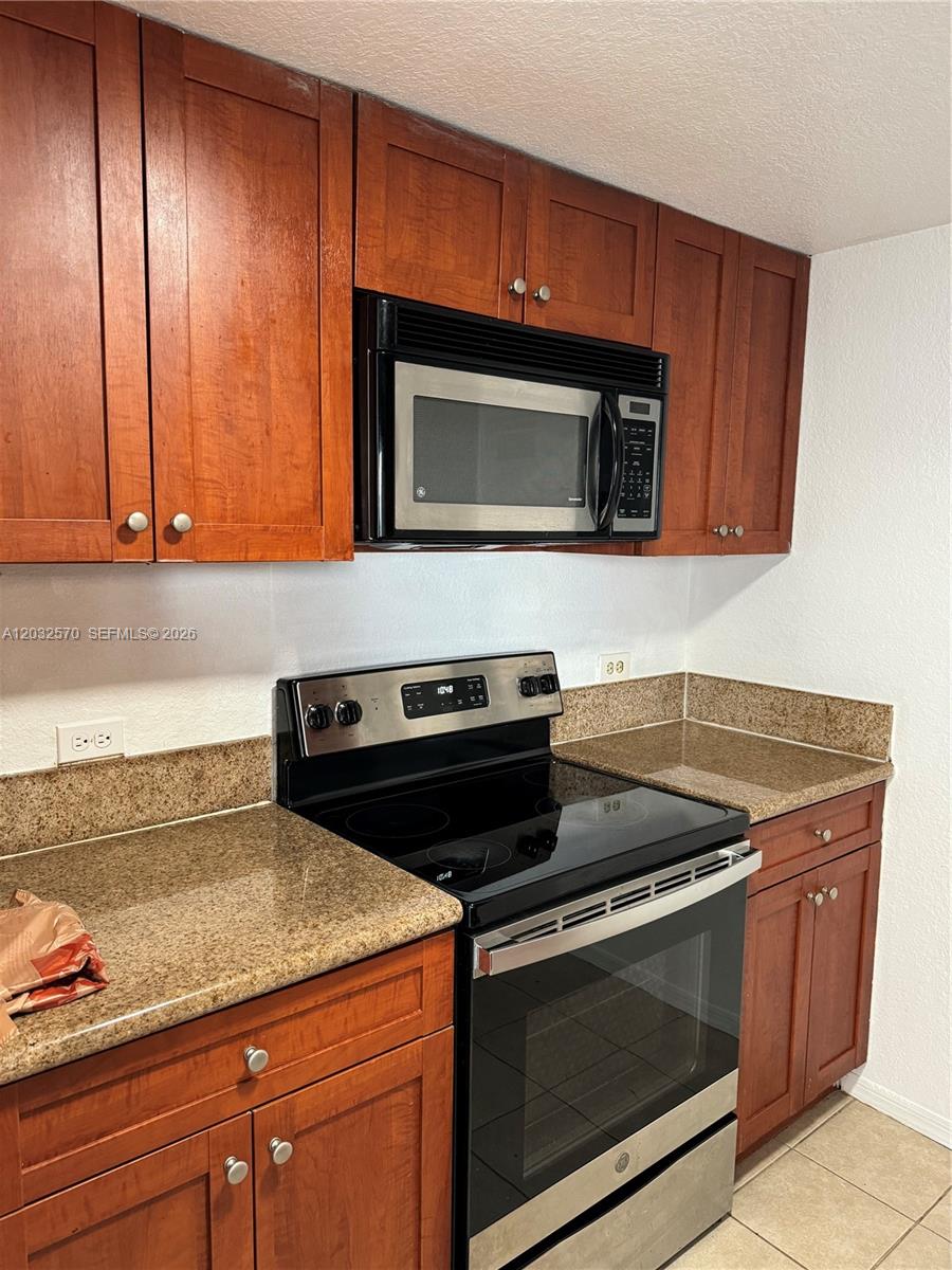 A kitchen features cherry-toned wooden cabinets, granite countertops, and stainless steel appliances — 36 NW 6th Ave # 601, Miami FL 33128, MIAMI, FL