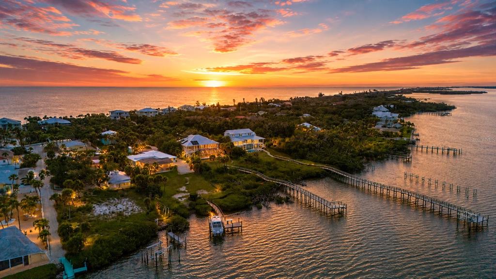 An aerial view of waterfront homes at sunset with private docks extending into the bay — 6065 MANASOTA KEY ROAD, ENGLEWOOD, FL