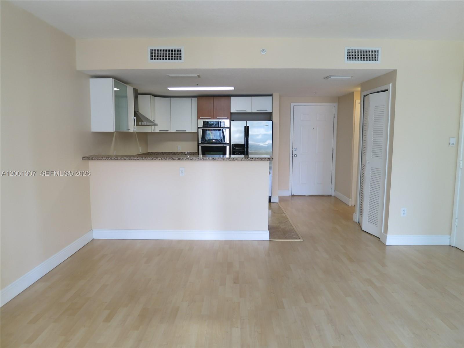 A kitchen with light wood flooring, granite countertops, and white cabinets opens to a living area — 170 SE 14 ST # 1507, Miami FL 33131, MIAMI, FL