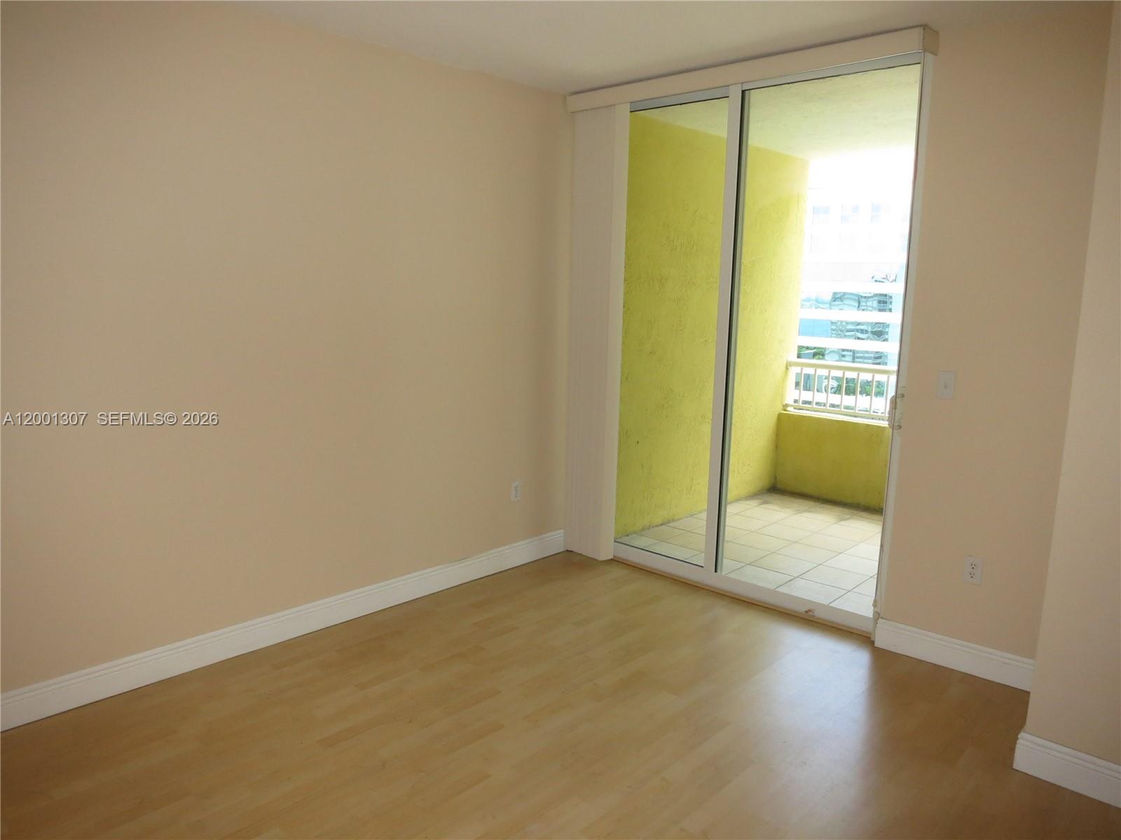 An empty room features light wood flooring, beige walls, and a sliding glass door to a balcony — 170 SE 14 ST # 1507, Miami FL 33131, MIAMI, FL