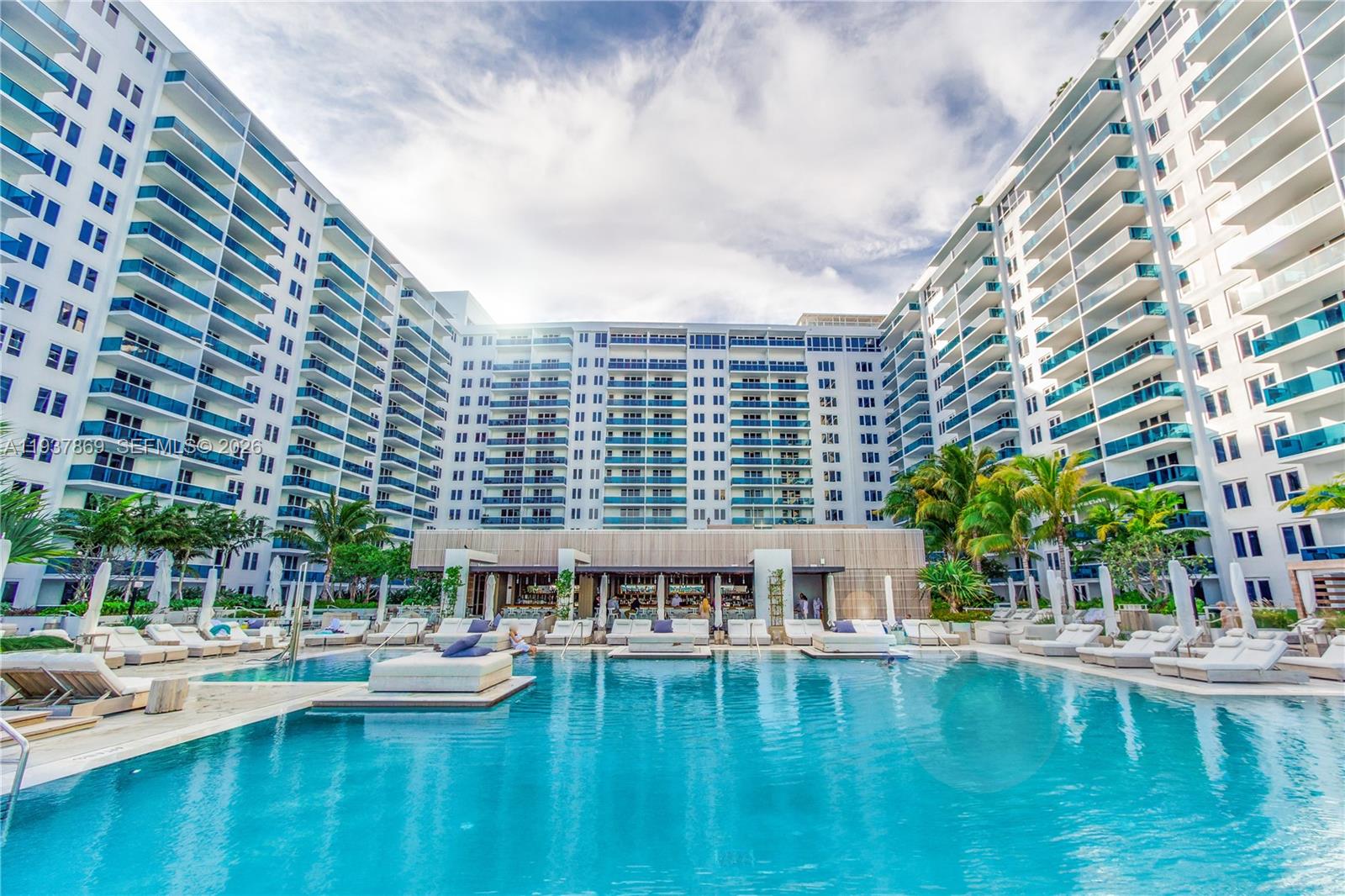 A large swimming pool sits in a courtyard surrounded by tall, modern white apartment buildings — 2301 COLLINS AV # 1026, Miami Beach FL 33139, MIAMI BEACH, FL