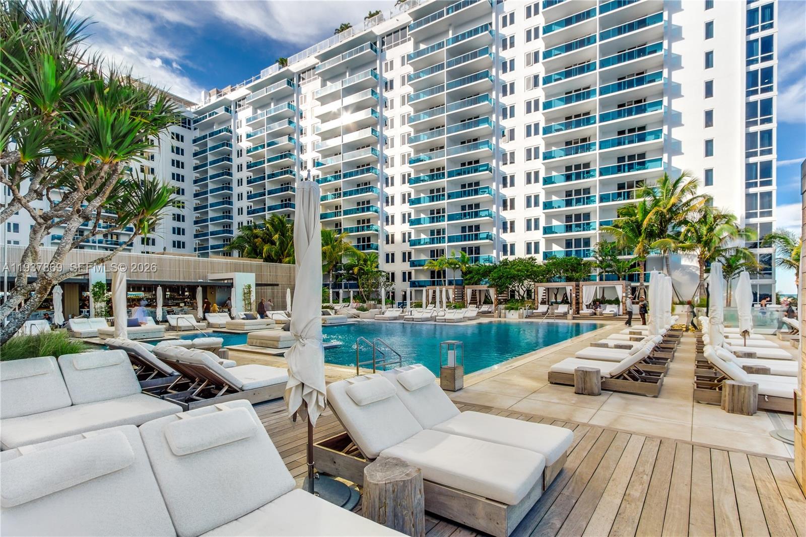 A swimming pool surrounded by lounge chairs and cabanas sits before a large apartment building — 2301 COLLINS AV # 1026, Miami Beach FL 33139, MIAMI BEACH, FL