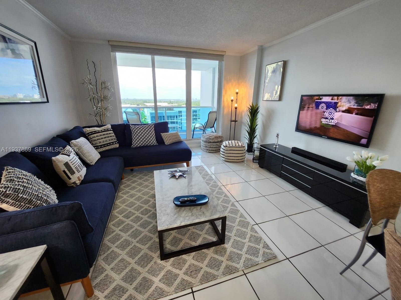 A living room features a navy sectional, marble coffee table, and a wall-mounted television — 2301 COLLINS AV # 1026, Miami Beach FL 33139, MIAMI BEACH, FL