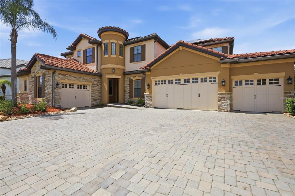 A large Mediterranean-style house features a paver driveway, a three-car garage, and a turret entrance — 5229 WATERSIDE VISTA LANE, ST CLOUD, FL