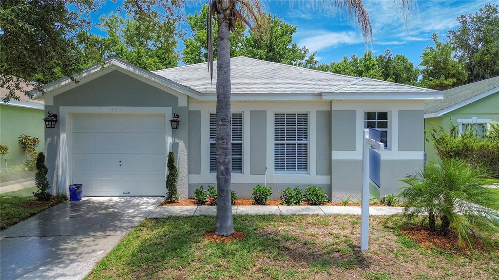 A single-story house with a white garage, gray stucco exterior, and a palm tree — 1501 ROYAL RIDGE DRIVE, DAVENPORT, FL