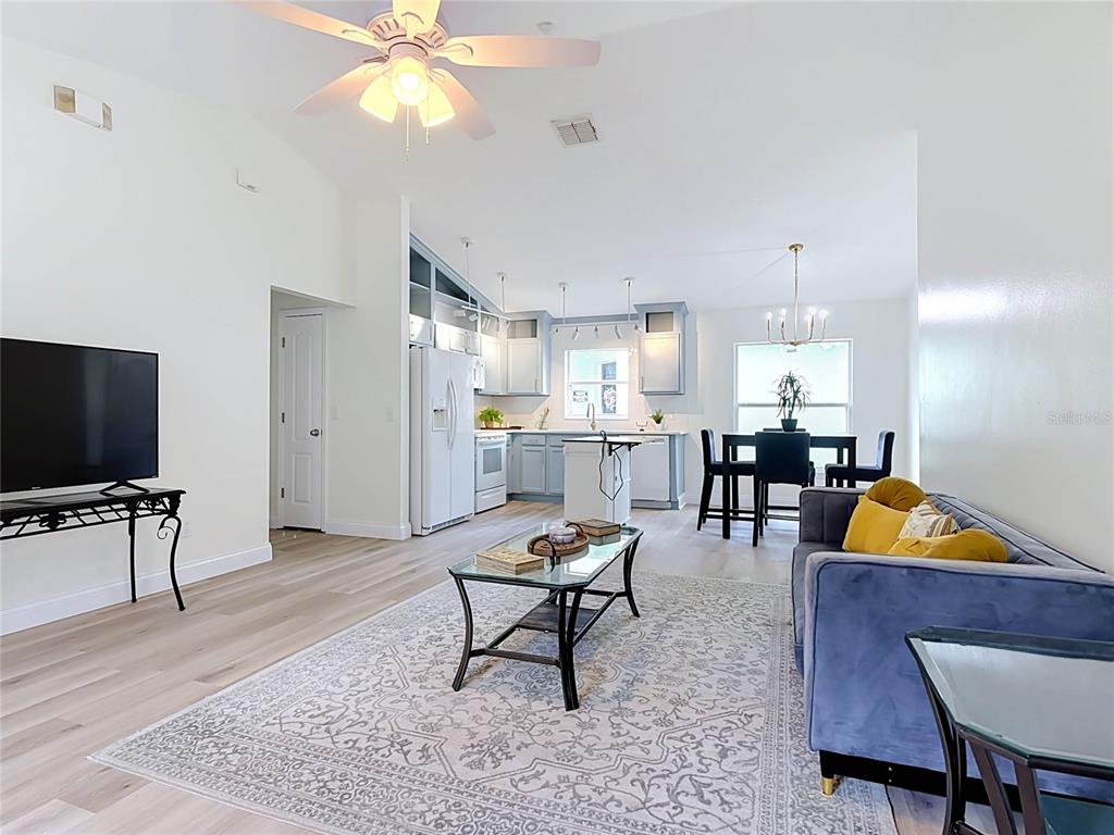 An open-concept living room and kitchen featuring light wood floors, a blue sofa, and cabinetry — 1501 ROYAL RIDGE DRIVE, DAVENPORT, FL