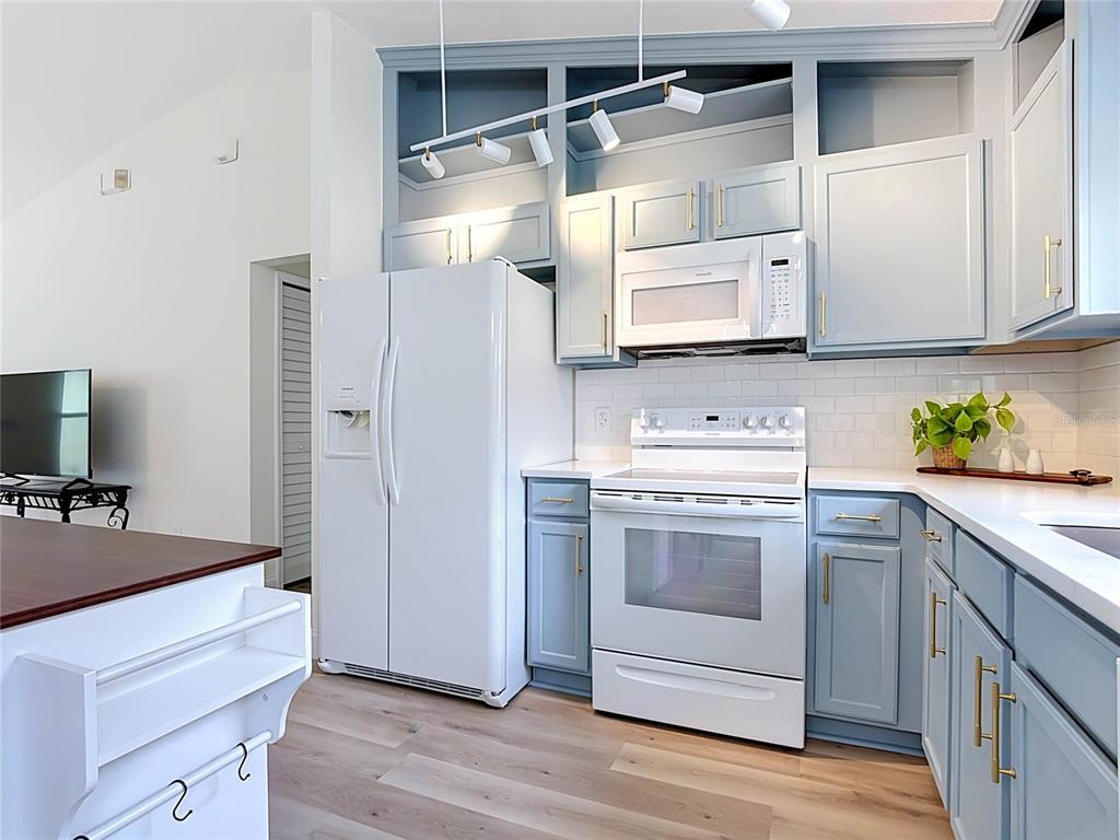 A kitchen features light blue cabinets, white appliances, a subway tile backsplash, and wood flooring — 1501 ROYAL RIDGE DRIVE, DAVENPORT, FL