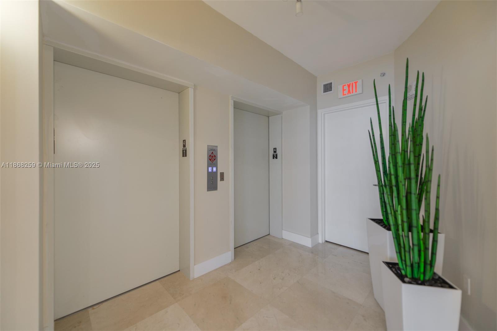 This indoor hallway features two elevator doors, an exit sign, and a tall potted plant — 3101 S Ocean Dr # 404, Hollywood FL 33019, HOLLYWOOD, FL