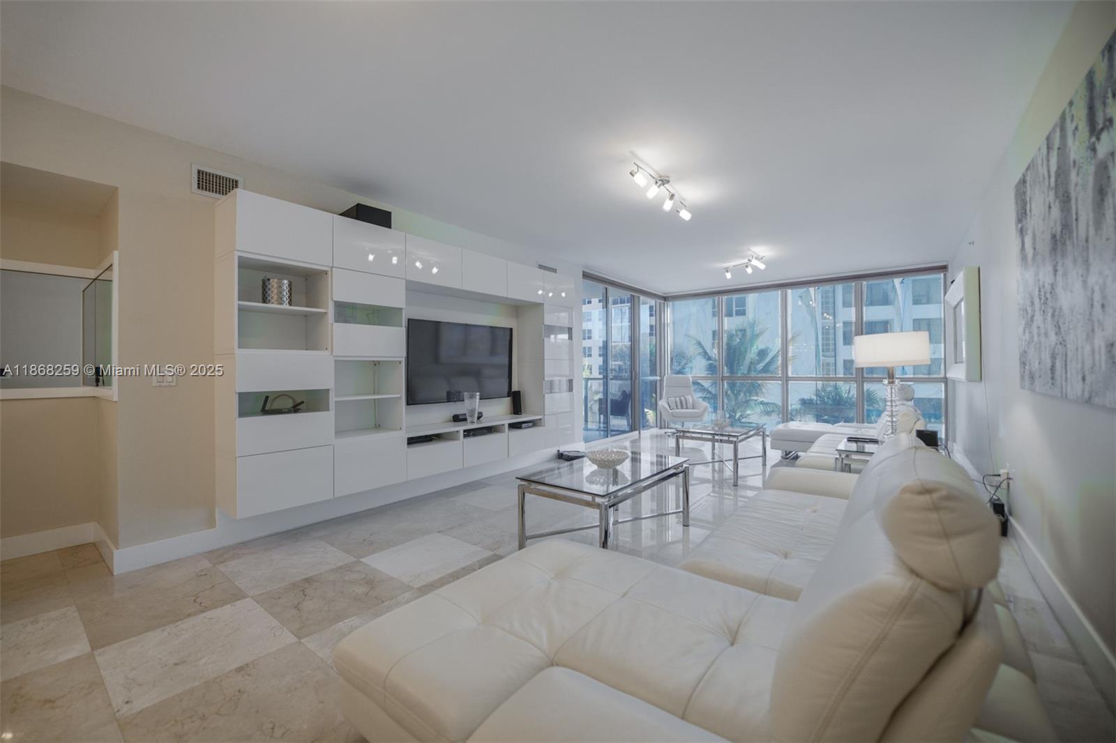 A modern living room features a white wall unit, leather sectional, and floor-to-ceiling windows — 3101 S Ocean Dr # 404, Hollywood FL 33019, HOLLYWOOD, FL