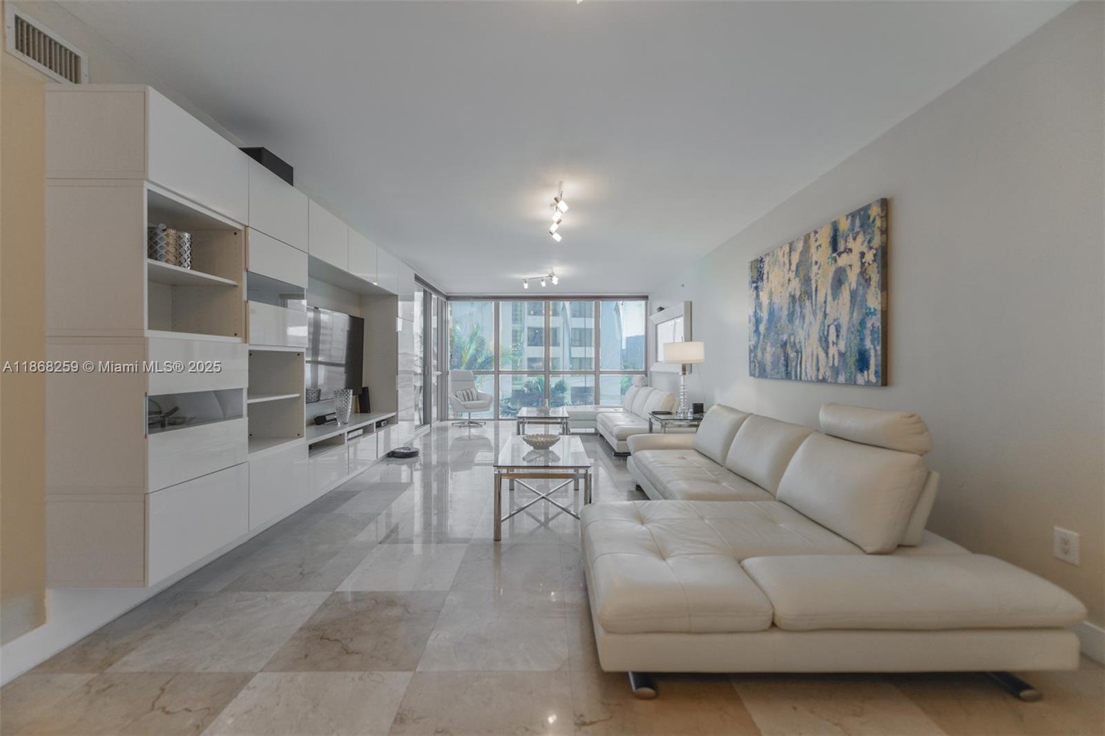 A modern living room features white leather sofas, a large wall unit, and marble flooring — 3101 S Ocean Dr # 404, Hollywood FL 33019, HOLLYWOOD, FL