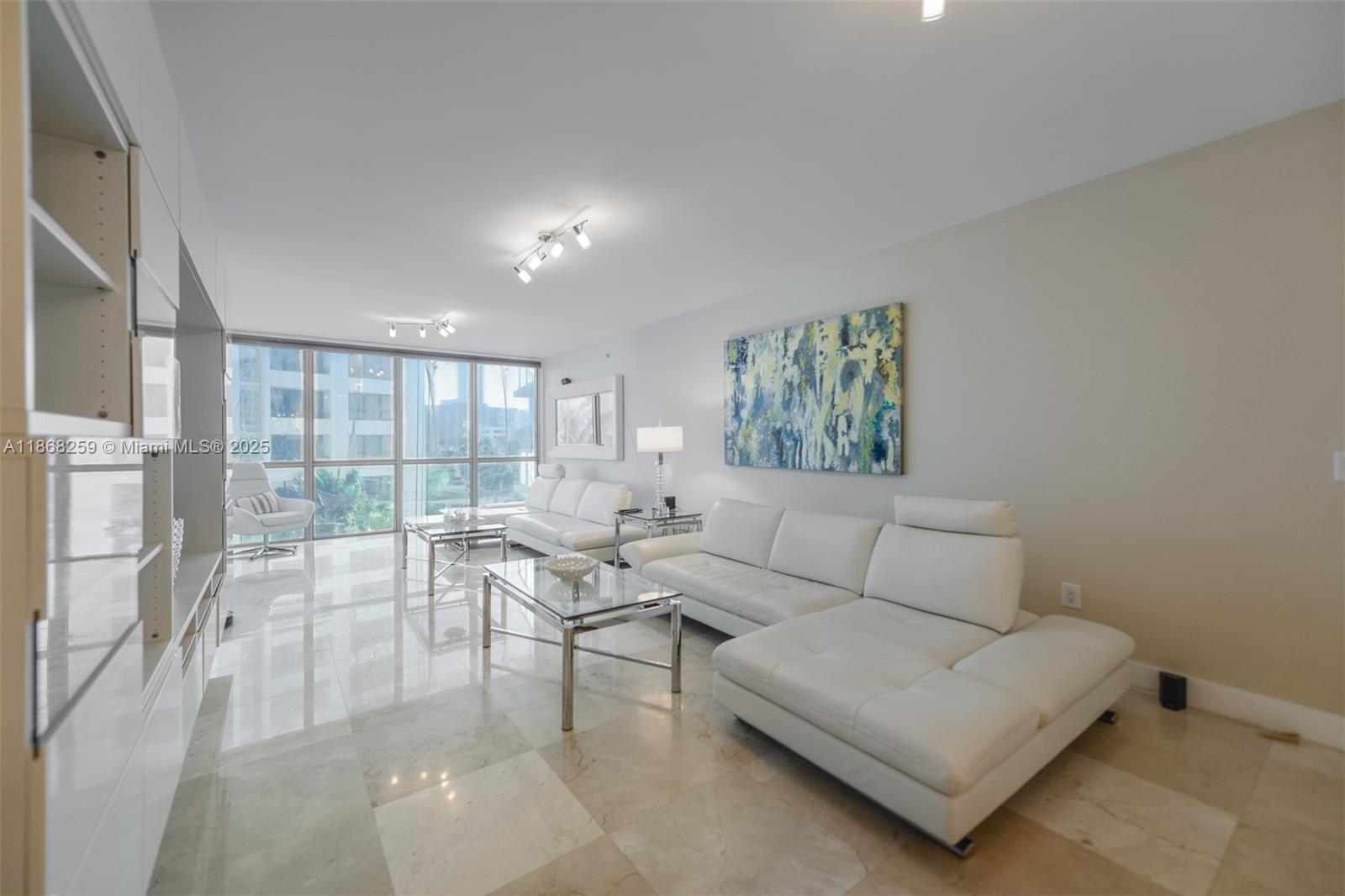 A bright living room features white leather sofas, glass coffee tables, and polished marble floors — 3101 S Ocean Dr # 404, Hollywood FL 33019, HOLLYWOOD, FL