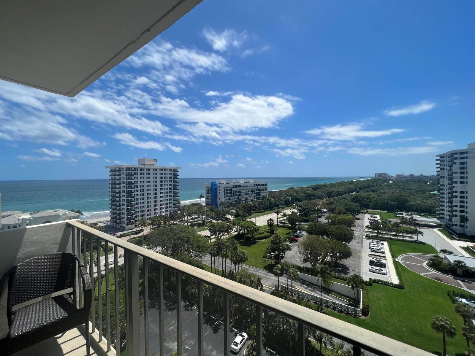 A high-angle view from a balcony overlooking a parking lot, green space, and the ocean — 2121 N Ocean Boulevard # 1405e, Boca Raton FL 33431, BOCA RATON, FL
