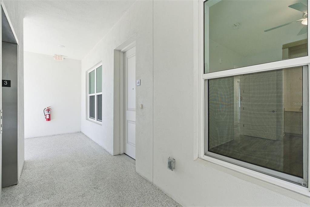A hallway with a white door, a window, an elevator, and a fire extinguisher — 400 150TH AVENUE UNIT 305, MADEIRA BEACH, FL