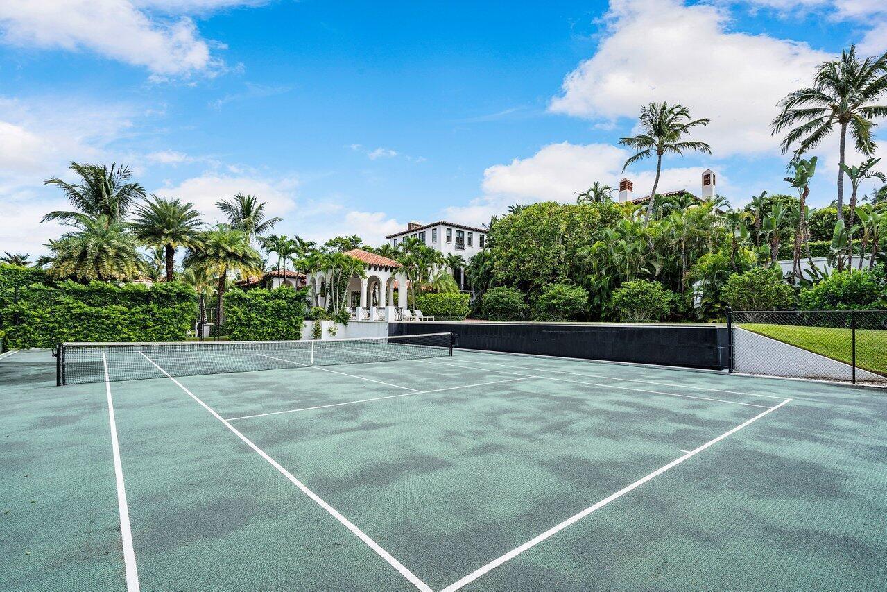 A tennis court with a net sits in front of a lush, tropical landscaped estate — 12 Lagomar Road, Palm Beach FL 33480, PALM BEACH, FL