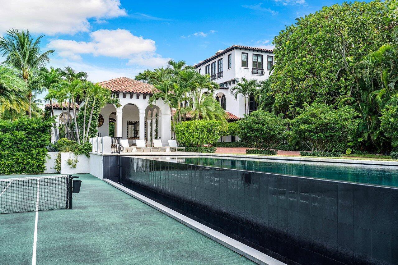 A tennis court sits beside a dark-tiled infinity pool in front of a Mediterranean-style villa — 12 Lagomar Road, Palm Beach FL 33480, PALM BEACH, FL