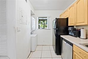 A kitchen features light wood cabinets, a black refrigerator, a dishwasher, and a laundry area — 504 Gardens Drive # 203, Pompano Beach FL 33069, POMPANO BEACH, FL