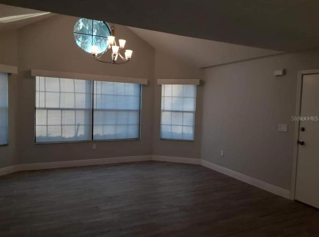 An empty room with vaulted ceilings, wood-look flooring, large windows with blinds, and a chandelier — 3123 FOX SQUIRREL DR UNIT B, KISSIMMEE, FL
