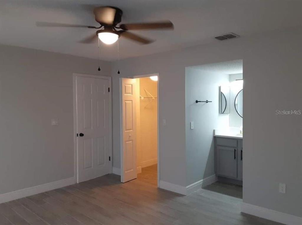 A bedroom with light gray walls, wood-look flooring, a ceiling fan, closet, and attached bathroom — 3123 FOX SQUIRREL DR UNIT B, KISSIMMEE, FL