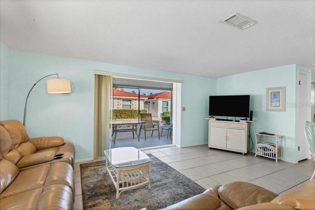 A living room with light blue walls, tile flooring, a leather sofa, and a sliding door — 6154 MIDNIGHT PASS ROAD UNIT D06, SARASOTA, FL