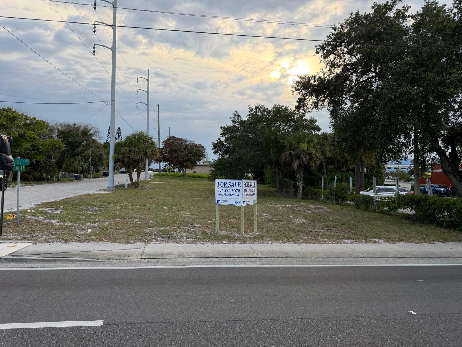 A vacant grassy lot with a for sale sign stands beside a paved road — 408 Avenue E, Fort Pierce FL 34950, FORT PIERCE, FL