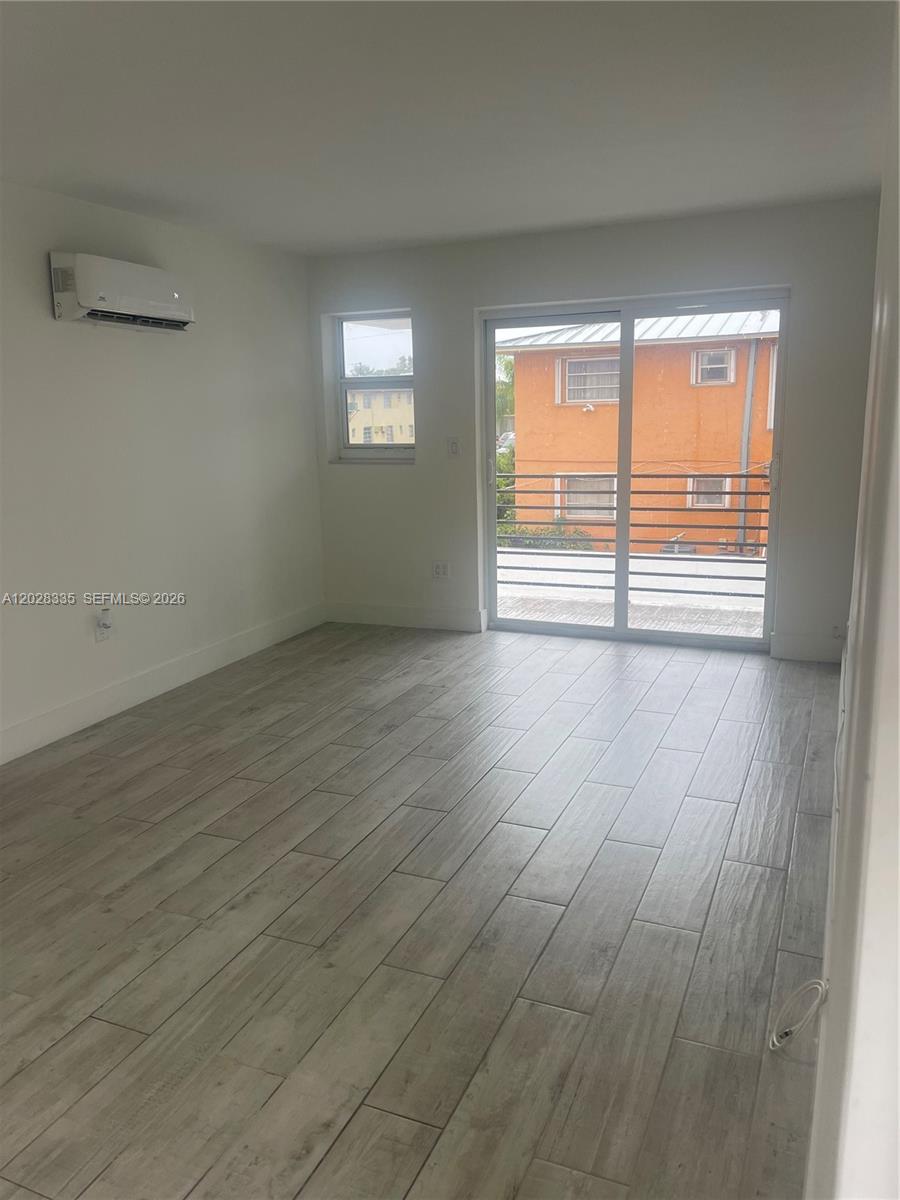 This room features light wood-look tile flooring, a wall-mounted air conditioner, and a sliding door — 2008 SW 3rd St # 4, Miami FL 33135, MIAMI, FL
