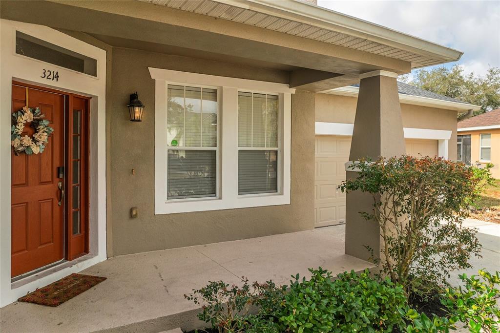 The exterior of a house features a tan stucco facade, a brown front door, and a porch — 3214 HOPEWELL DRIVE, KISSIMMEE, FL