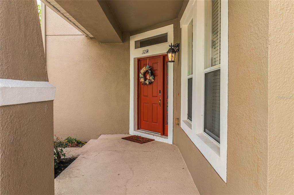 A red front door with a wreath sits under a covered porch with beige walls — 3214 HOPEWELL DRIVE, KISSIMMEE, FL