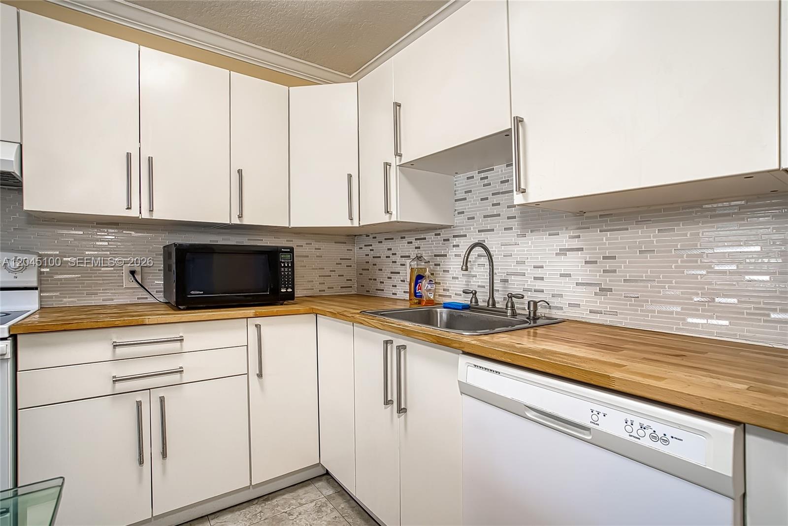 A kitchen features white cabinets, a wood countertop, a stainless steel sink, and tiled backsplash — 173 Ellesmere C # 173, Deerfield Beach FL 33442, DEERFIELD BEACH, FL