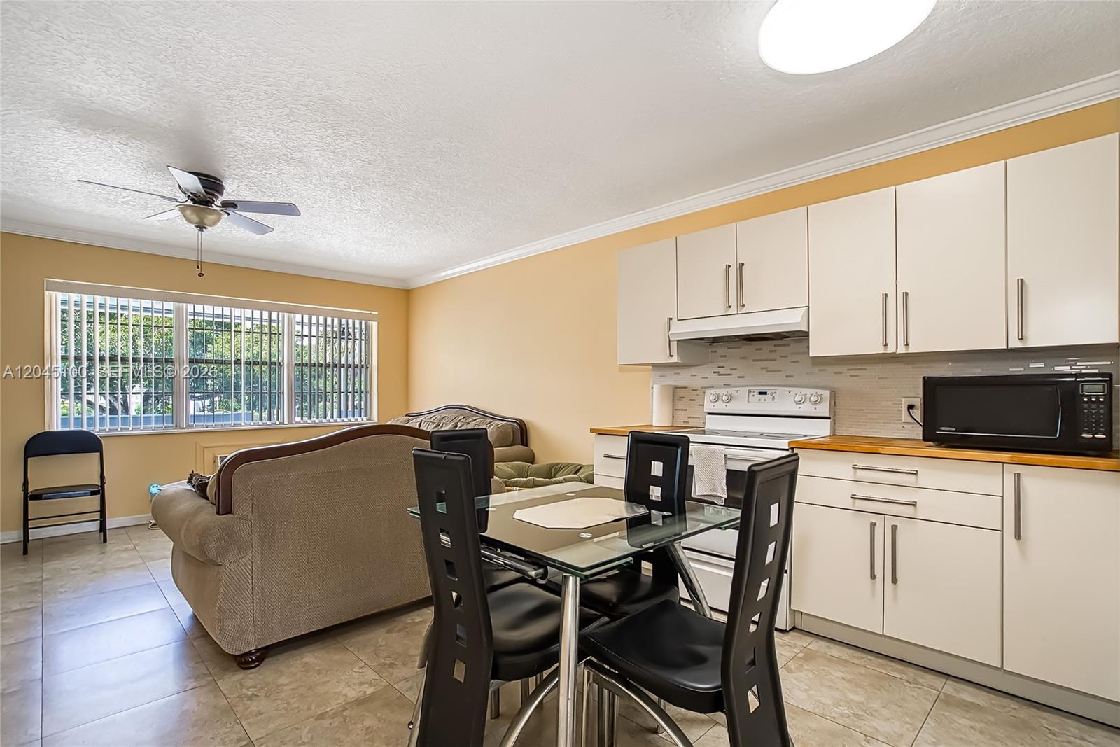 A kitchen and dining area features white cabinets, a glass table, and a living space — 173 Ellesmere C # 173, Deerfield Beach FL 33442, DEERFIELD BEACH, FL