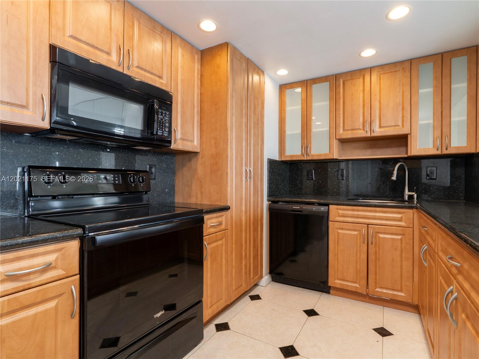 A kitchen features light wood cabinets, black appliances, dark granite countertops, and tiled flooring — 11111 Biscayne Blvd # 912, Miami FL 33181, MIAMI, FL
