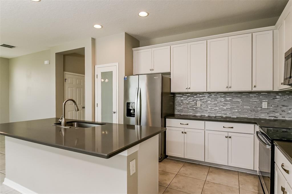 A kitchen features white cabinets, dark countertops, a stainless steel refrigerator, and a center island — 10313 BERRYESSA AVENUE, RIVERVIEW, FL