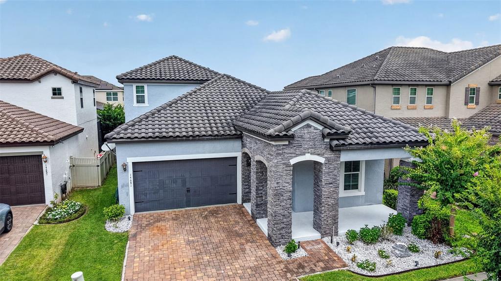 A single-story house features a gray stone facade, a tiled roof, and a brick driveway — 14681 SETON CREEK BOULEVARD, WINTER GARDEN, FL