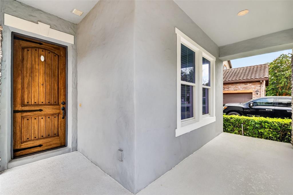 A covered front porch features a wooden door, a window, and light gray stucco walls — 14681 SETON CREEK BOULEVARD, WINTER GARDEN, FL
